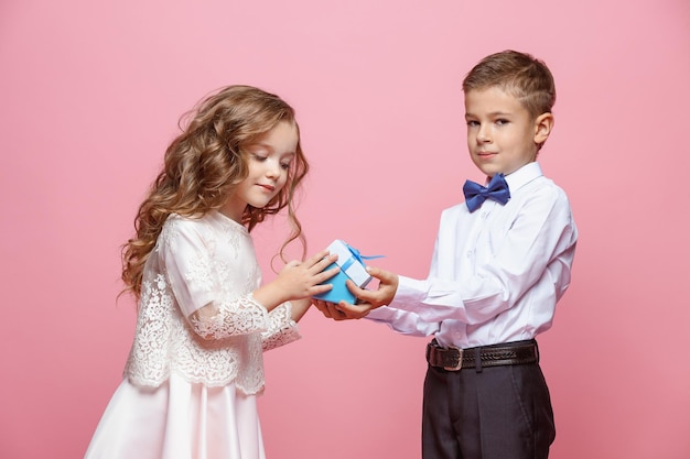 Ragazzo e ragazza in piedi e in posa con regalo in studio su rosa