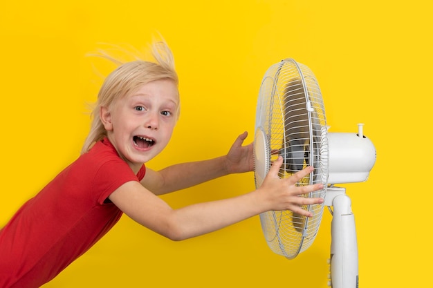 Ragazzo e ventilatore su sfondo giallo Il bambino si raffredda con il ventilatore quando fa caldo