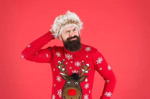 Ragazzo emotivo. Previsioni del tempo. Moda invernale. Cura invernale. Giorni freddi. Umore invernale. I pantaloni a vita bassa barbuti indossano un maglione lavorato a maglia e un cappello di pelliccia. Servizi di barbiere. Uomo con barba e baffi lunghi.