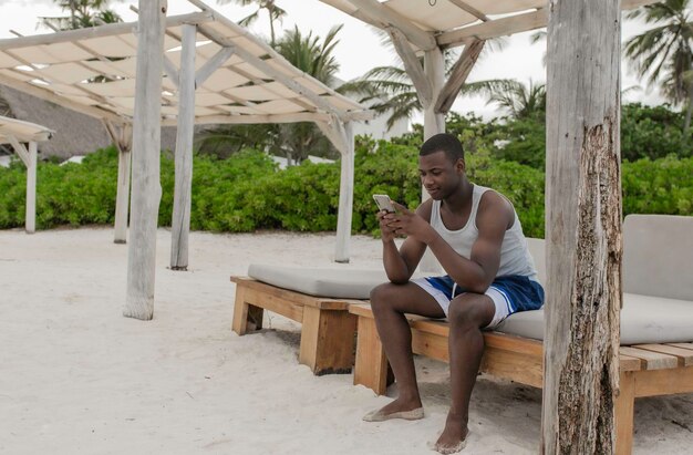 Ragazzo etnico che utilizza il telefono cellulare sulla panchina in terrazza tropicale