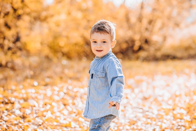 Ragazzo felice che gioca con le foglie gialle autunnali all'aperto nel parco