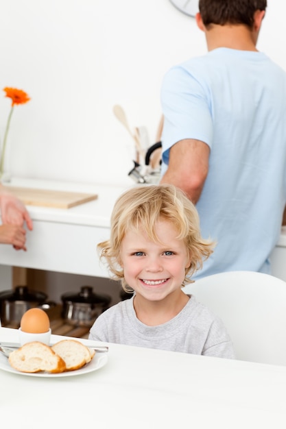 Ragazzo felice che mangia uovo bollito e pane in cucina