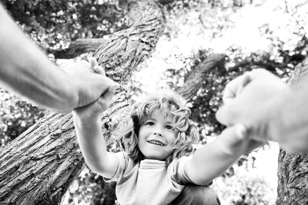 Ragazzo felice che si arrampica su un albero durante l'ora legale Mano dei padri