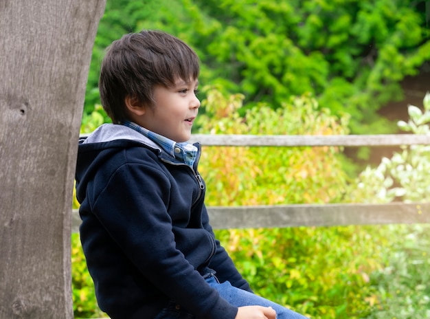 Ragazzo felice che si siede sul banco di legno con la faccia sorridente nel parco