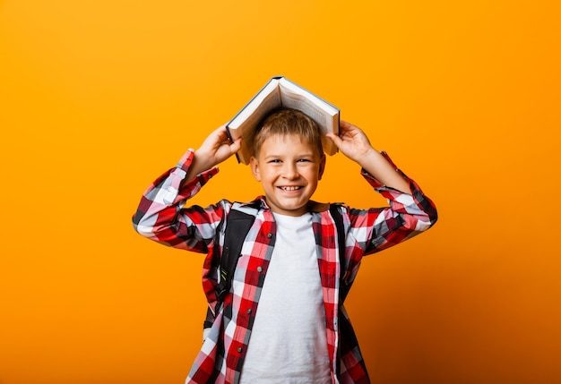 Ragazzo felice che sorride alla telecamera e tiene dei libri sulla testa, su uno sfondo giallo