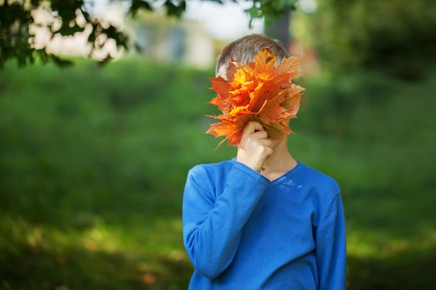 ragazzo felice che tiene il mazzo di foglie di acero arancione