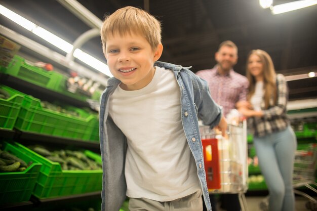 Ragazzo felice che tira carrello in supermercato