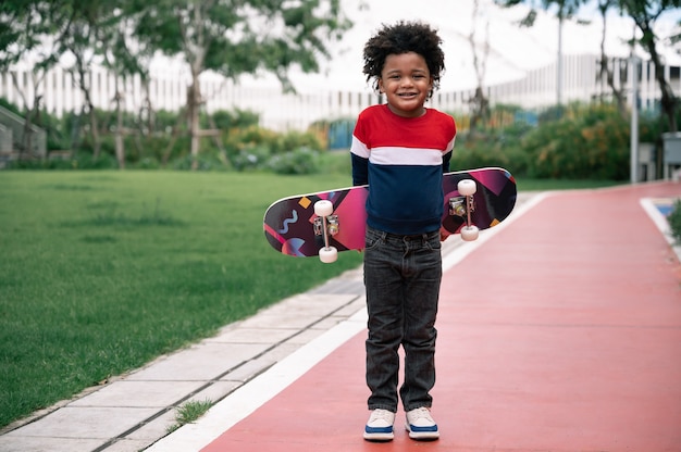 Ragazzo felice con capelli afro e skateboard nel parco