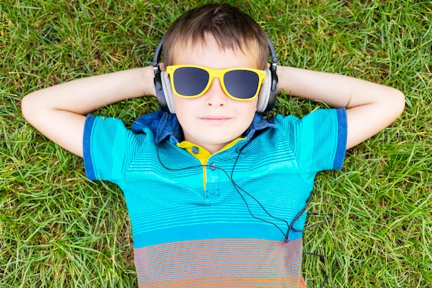 Ragazzo felice con gli occhiali da sole sdraiato sull'erba e che ascolta musica con le cuffie