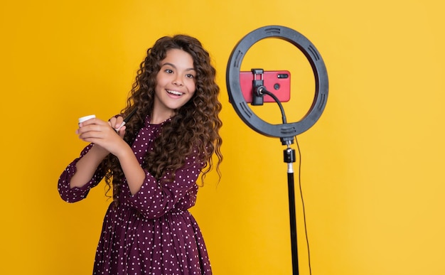 Ragazzo felice con lunghi capelli ricci che fa video per il pennello da cipria da tenere sul blog