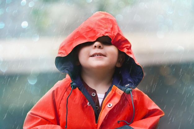 Ragazzo felice impermeabile rosso e bambino piccolo che gioca o si diverte con le gocce di pioggia e all'aperto Sorridi bambino e guarda il cielo o goditi la pioggia e le docce su sfondo bokeh