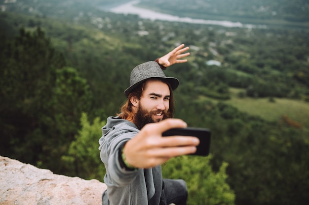 Ragazzo felice in alta montagna utilizzando un telefono cellulare prende un selfie.