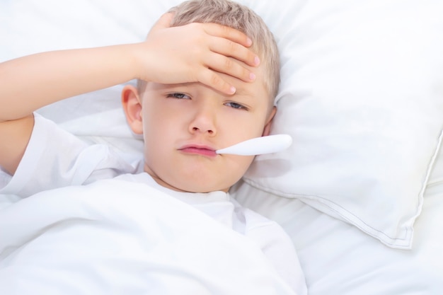 Ragazzo giace a letto con un termometro in bocca. concetto sanitario e bambino malato, coronavirus, febbre alta,
