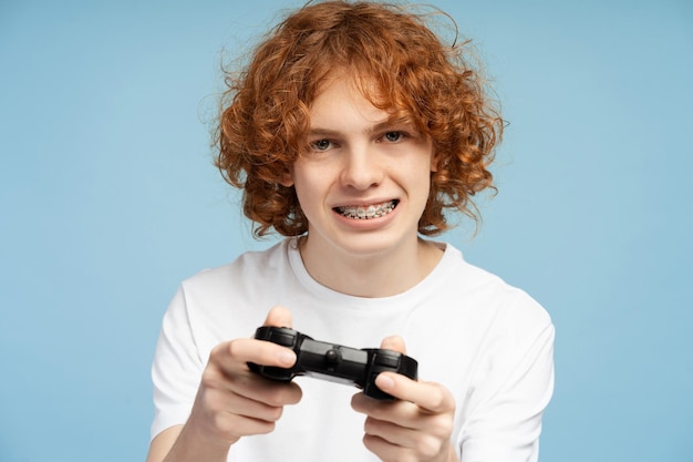 Ragazzo ginger curly che gioca a videogiochi usando un joystick su uno sfondo blu isolato