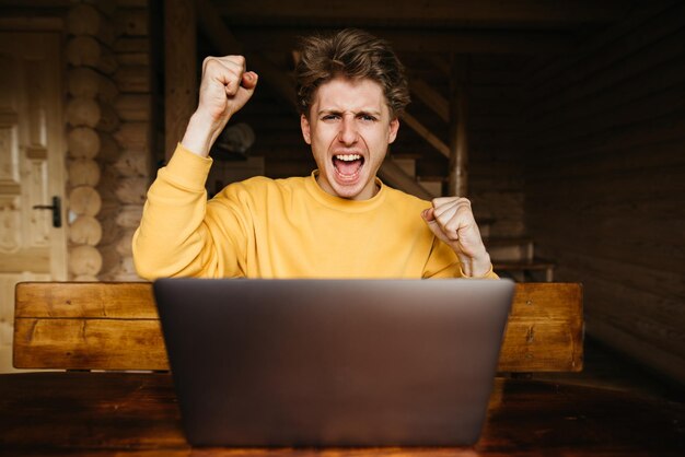 Ragazzo gioioso con una felpa arancione usa un laptop in una casa di campagna con interni in legno