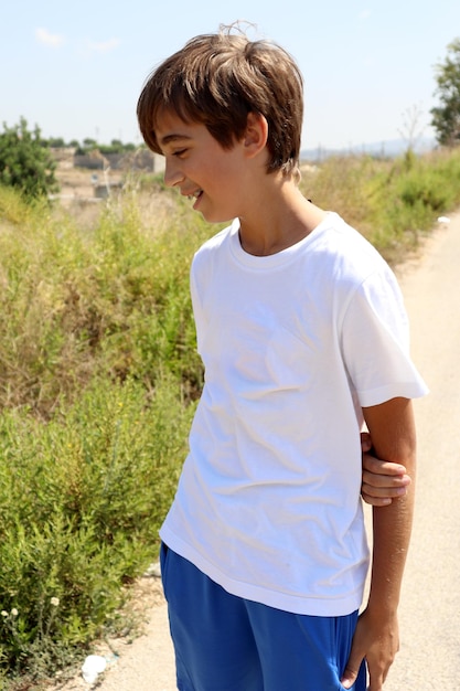 Ragazzo giovane biondo in camicia bianca e pantaloncini blu che si gode il sole estivo in natura