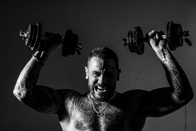 Ragazzo giovane bodybuilder muscolare facendo esercizi con manubri su sfondo scuro Allenamento intenso