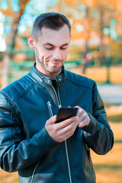 Ragazzo giovane che usa uno smartphone nero nel bellissimo parco autunnale