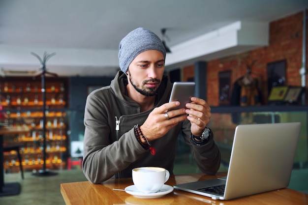 Ragazzo giovane e bello dei pantaloni a vita bassa al ristorante usando un telefono cellulare