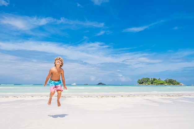 Ragazzo giovane salti di gioia sulla spiaggia tropicale, concetto di vacanza estiva