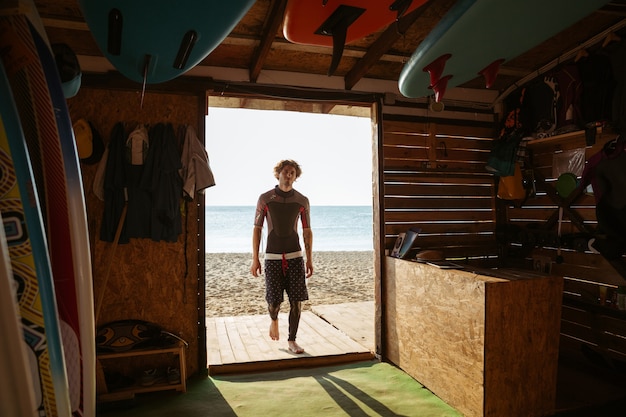 Ragazzo giovane surfista stanco andando alla capanna di surf in spiaggia