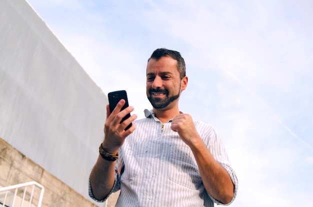 Ragazzo guardando cellulare, felice lettura di buone notizie. L&#39;uomo riceve risposta positiva su smart pho