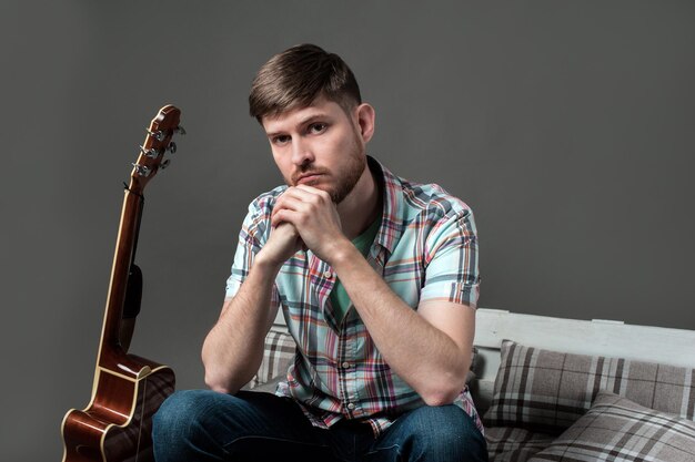 Ragazzo hipster che indossa occhiali da sole e tiene la sua chitarra in riva al lago