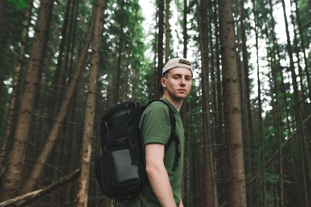 Ragazzo hipster con zaino escursionismo in montagna su sfondo scuro della foresta