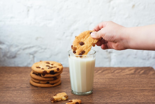 Ragazzo immersione gustoso biscotto in un bicchiere di latte Gustosi biscotti fatti in casa profumati con uvetta e un bicchiere di latte fresco