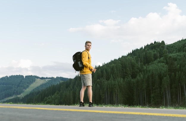 ragazzo in abiti casual arancione si trova su una strada di montagna su uno sfondo di foresta di conifere