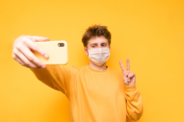 Ragazzo in abiti casual e maschera bianca medica fa selfie con la faccia seria sullo smartphone