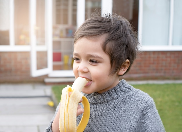 Ragazzo in buona salute che mangia banana fresca con un fadein felice il giardino