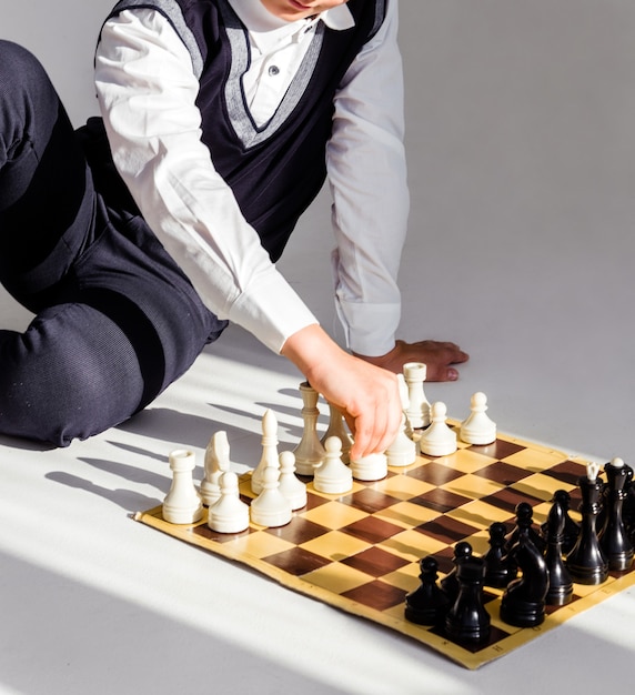 Ragazzo in camicia bianca e gilet nero gioca a scacchi mentre è seduto sul pavimento alla luce del sole