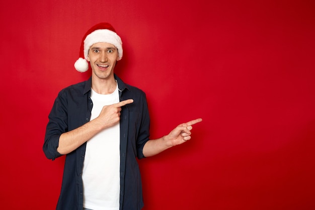 Ragazzo in cappello di babbo natale capodanno punta con due dita indice in un vuoto isolato su sfondo rosso