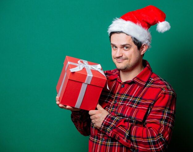 Ragazzo in cappello di Natale e camicia in tartan con confezione regalo su verde