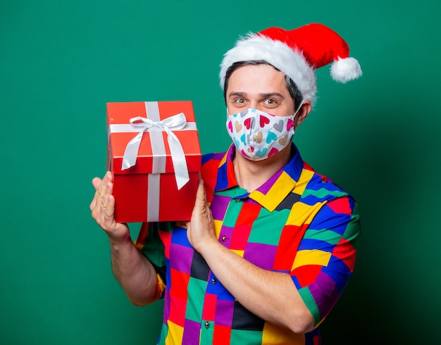 Ragazzo in cappello di Natale e camicia vintage che tiene un regalo sul verde