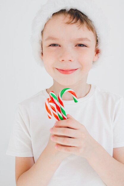 Ragazzo in cappello rosso della Santa che tiene un bastoncino di zucchero