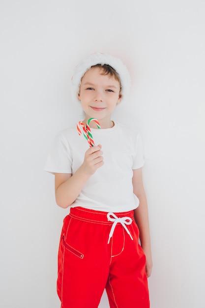 Ragazzo in cappello rosso della Santa che tiene un bastoncino di zucchero