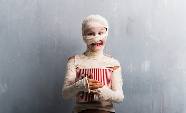 Ragazzo in costume della mummia che mangia i popcorn per le feste di Halloween