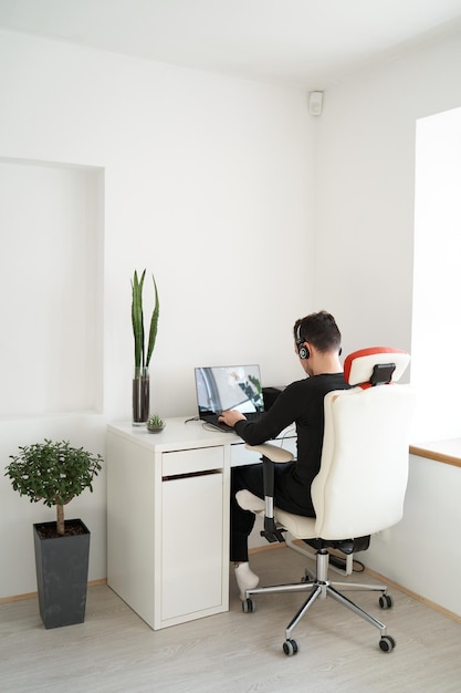 Ragazzo in cuffia che lavora al computer portatile in interni chiari