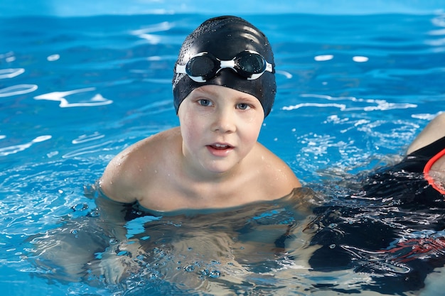 Ragazzo in età prescolare che impara a nuotare in una piscina con cuffia e occhiali
