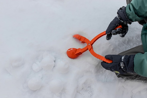 Ragazzo in guanti caldi detiene un dispositivo per fare palle di neve. giochi attivi invernali. copia spazio