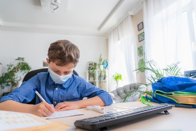 Ragazzo in maschera con il computer, facendo i compiti durante la quarantena di coronavirus