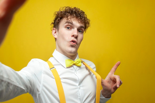 Ragazzo in papillon e bretelle scatta selfie su sfondo giallo il nerd si fotografa