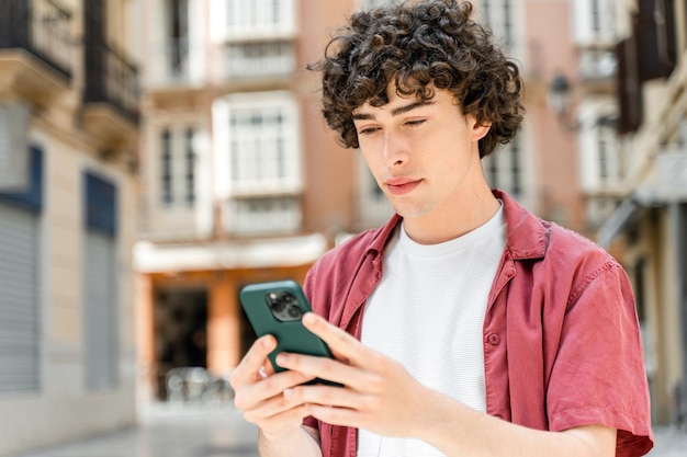 Ragazzo in piedi per strada e messaggistica con gli amici al suo smartphone