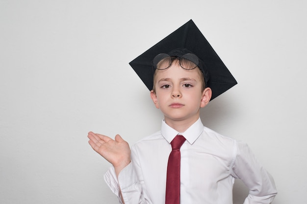 Ragazzo in un cappello accademico quadrato e occhiali regge il palmo della mano. Concetto di scuola.