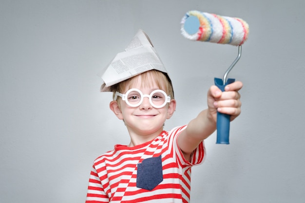 Ragazzo in un cappello di carta e occhiali. Piccolo pittore. Ritratto. Rullo per pittura