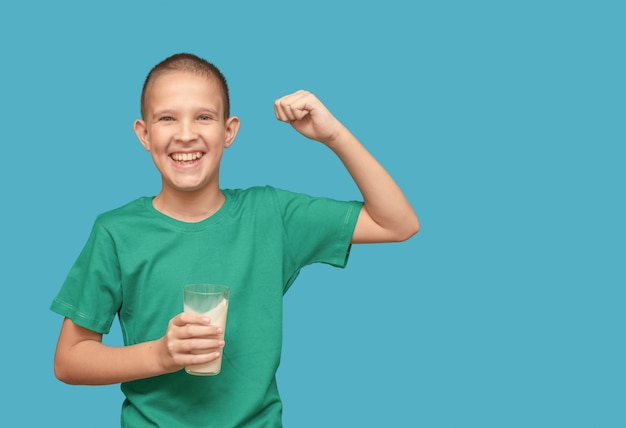 Ragazzo in una maglietta verde con un bicchiere di latte sorriso felice su sfondo blu.