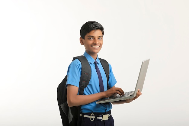 Ragazzo indiano della scuola in uniforme e usando il computer portatile su fondo bianco