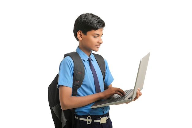 Ragazzo indiano della scuola in uniforme e usando il computer portatile su fondo bianco